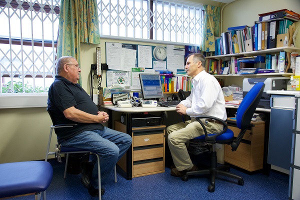 White male GP talks with White male patient in general practice consulting room